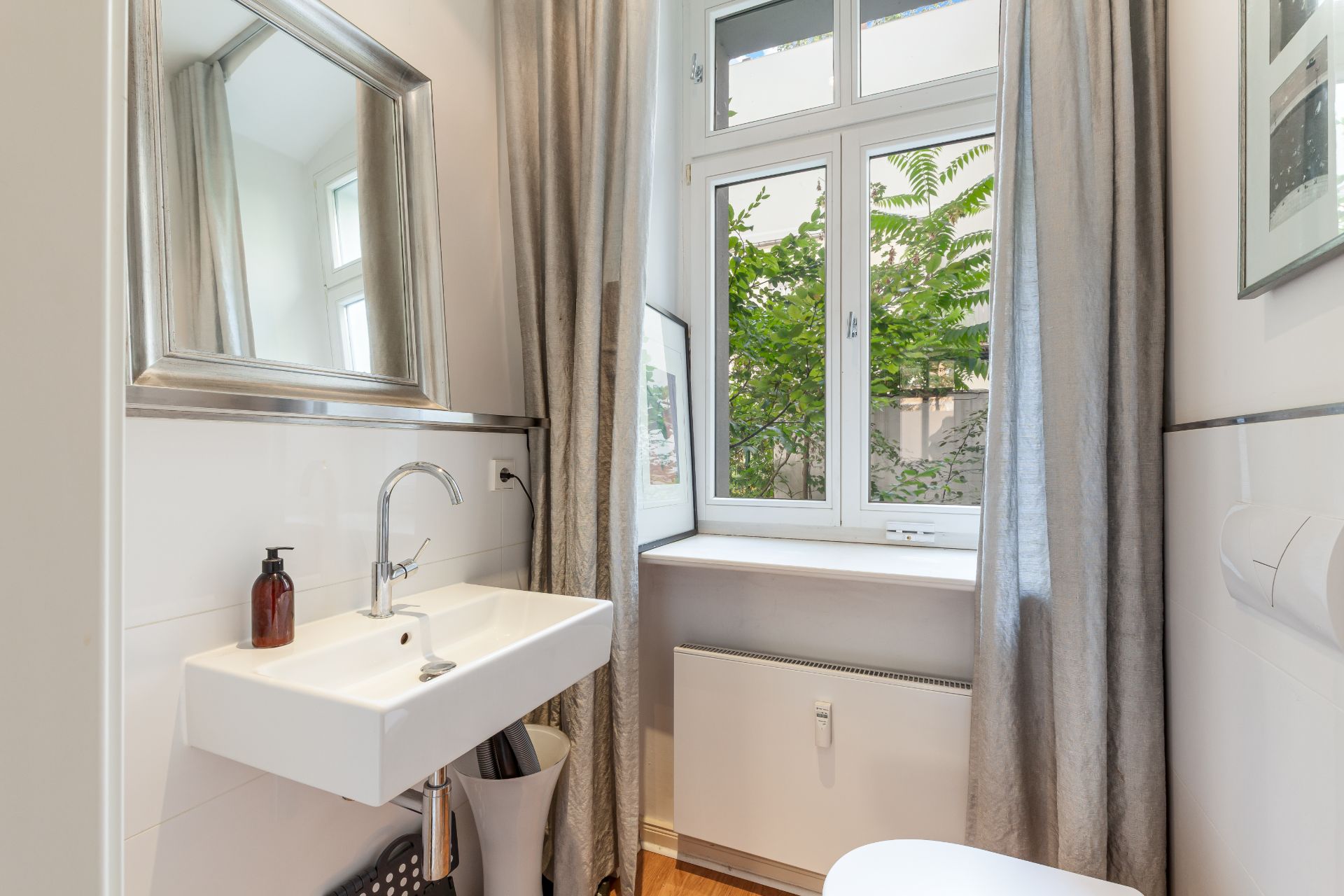 Kleines Badezimmer mit Waschbecken, Spiegel, Fenster und grauen Vorhängen.