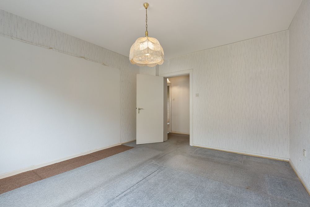 Leerer Raum mit Teppichboden, Deckenlampe und geöffneter Tür, helle Wände.
