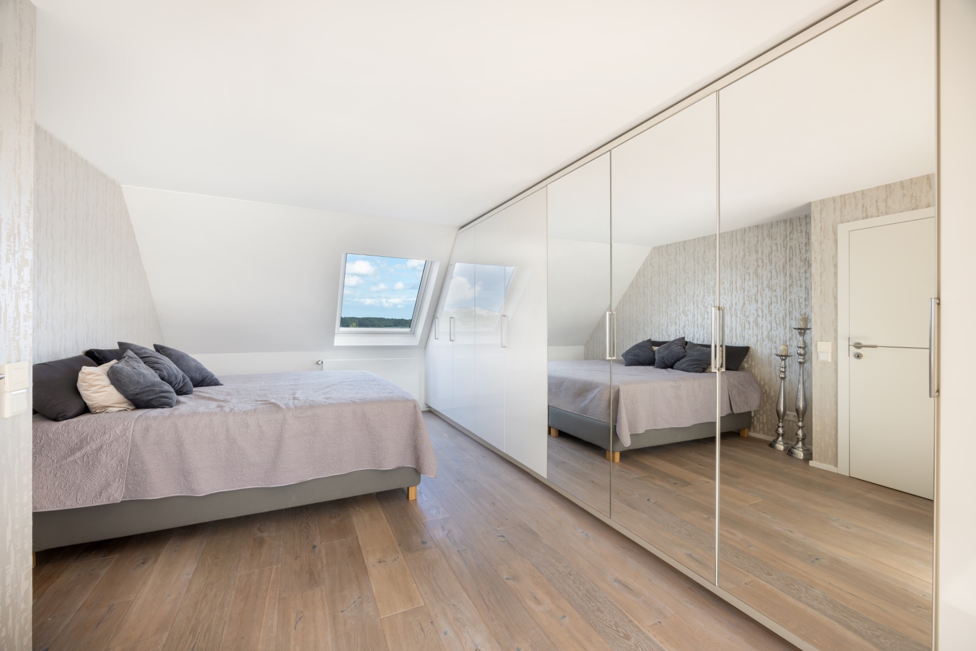 Helles Schlafzimmer mit Doppelbett, großem Spiegelschrank und Fenster mit Ausblick.