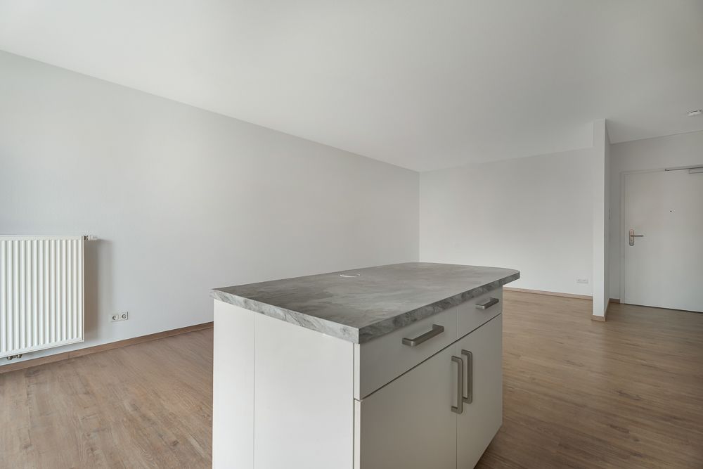 Helles Zimmer mit Holzboden und Kücheninsel, weißer Wand und Heizkörper.