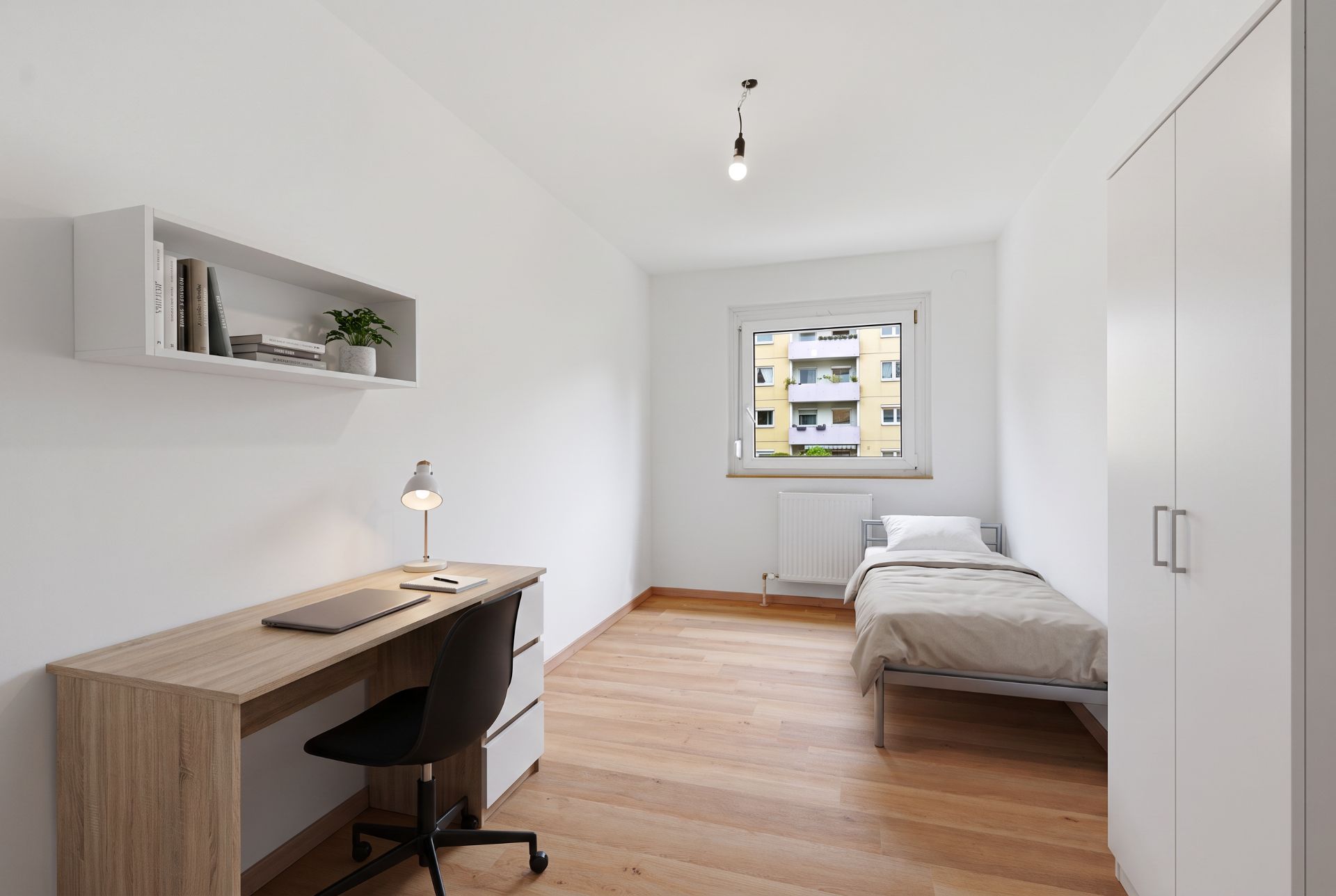 Helles Schlafzimmer mit Einzelbett, Schreibtisch, Stuhl und großem Schrank, Holzfußboden.