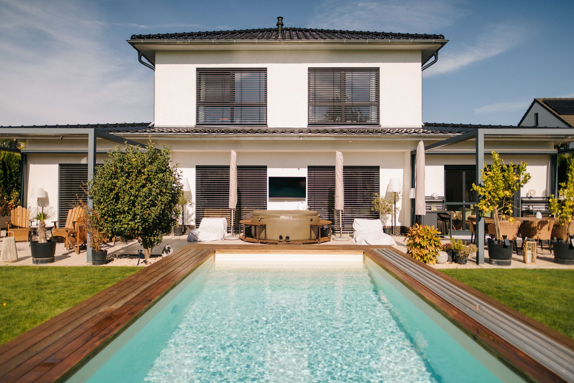 Modernes weißes Haus mit Pool im Garten und großer Terrasse mit Sitzmöbeln.
