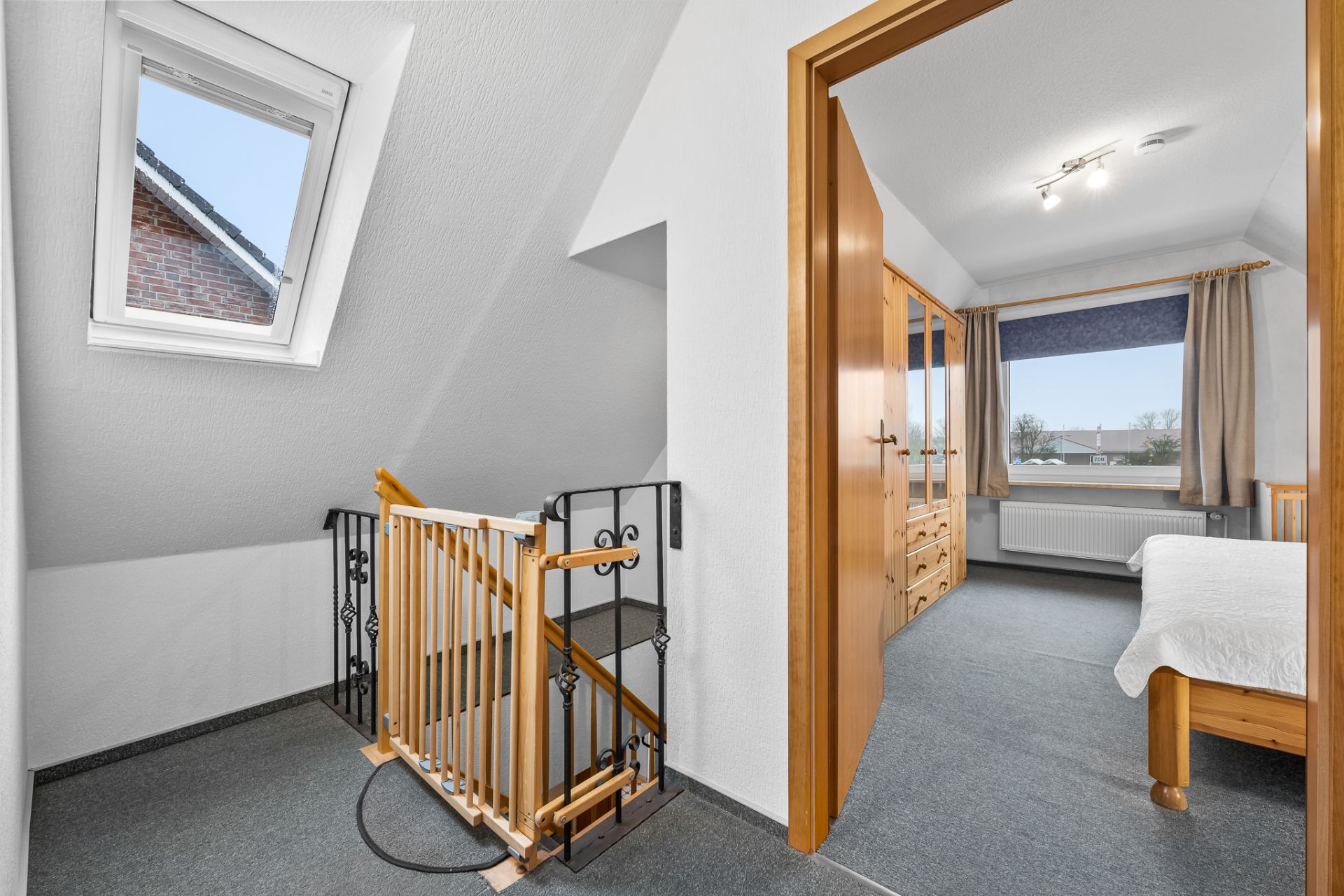 Flur mit Treppenschutzgitter und Blick in ein Schlafzimmer mit großem Fenster.