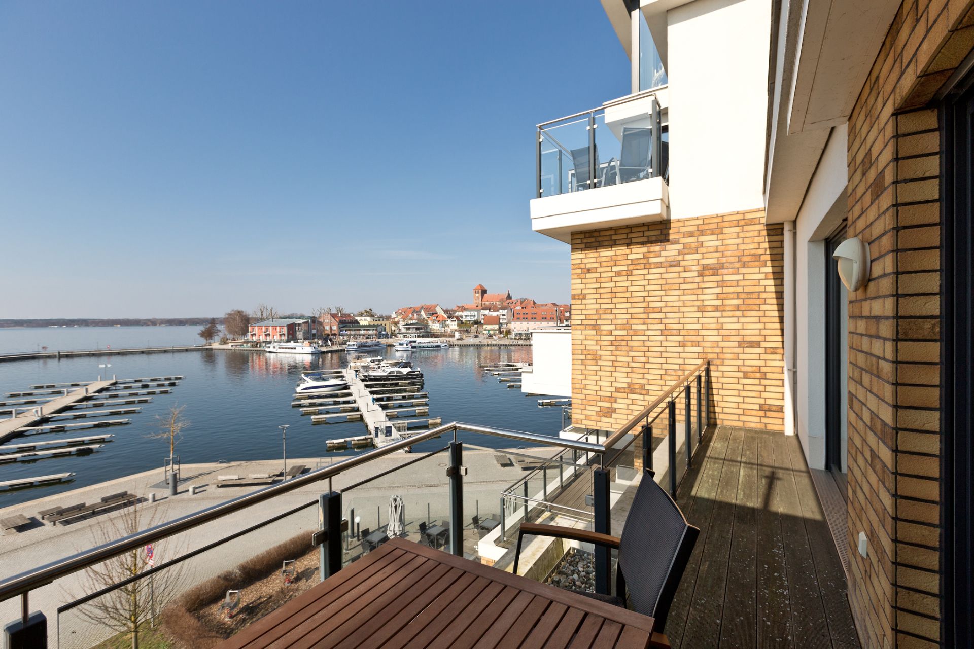 Balkon mit Holztisch und Blick auf einen Yachthafen und Wasser.