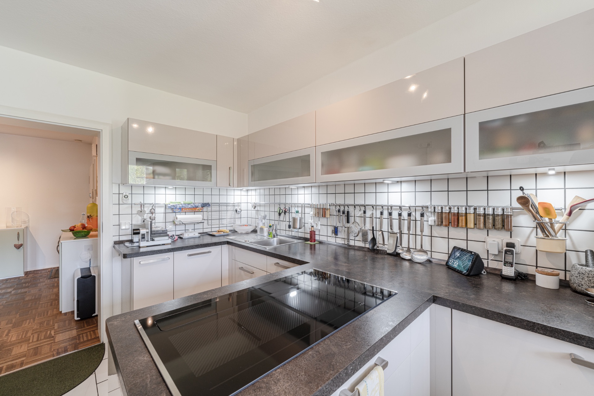 Moderne Wohnküche mit Kochfeld, weißen Schränken und Küchenutensilien an der Wand.