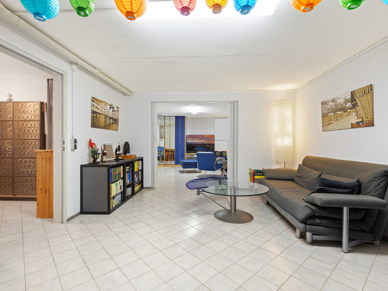 Helles Wohnzimmer mit Sofa, Glastisch, Bücherregal und bunten Lampions an der Decke.