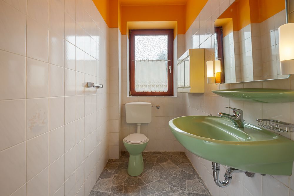 Kleines Badezimmer mit grünem Waschbecken, grünem WC, Fenster und weiß gefliesten Wänden.