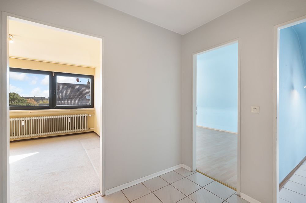 Heller Flur mit Blick in zwei angrenzende Zimmer, eines mit großem Fenster und Heizkörper.