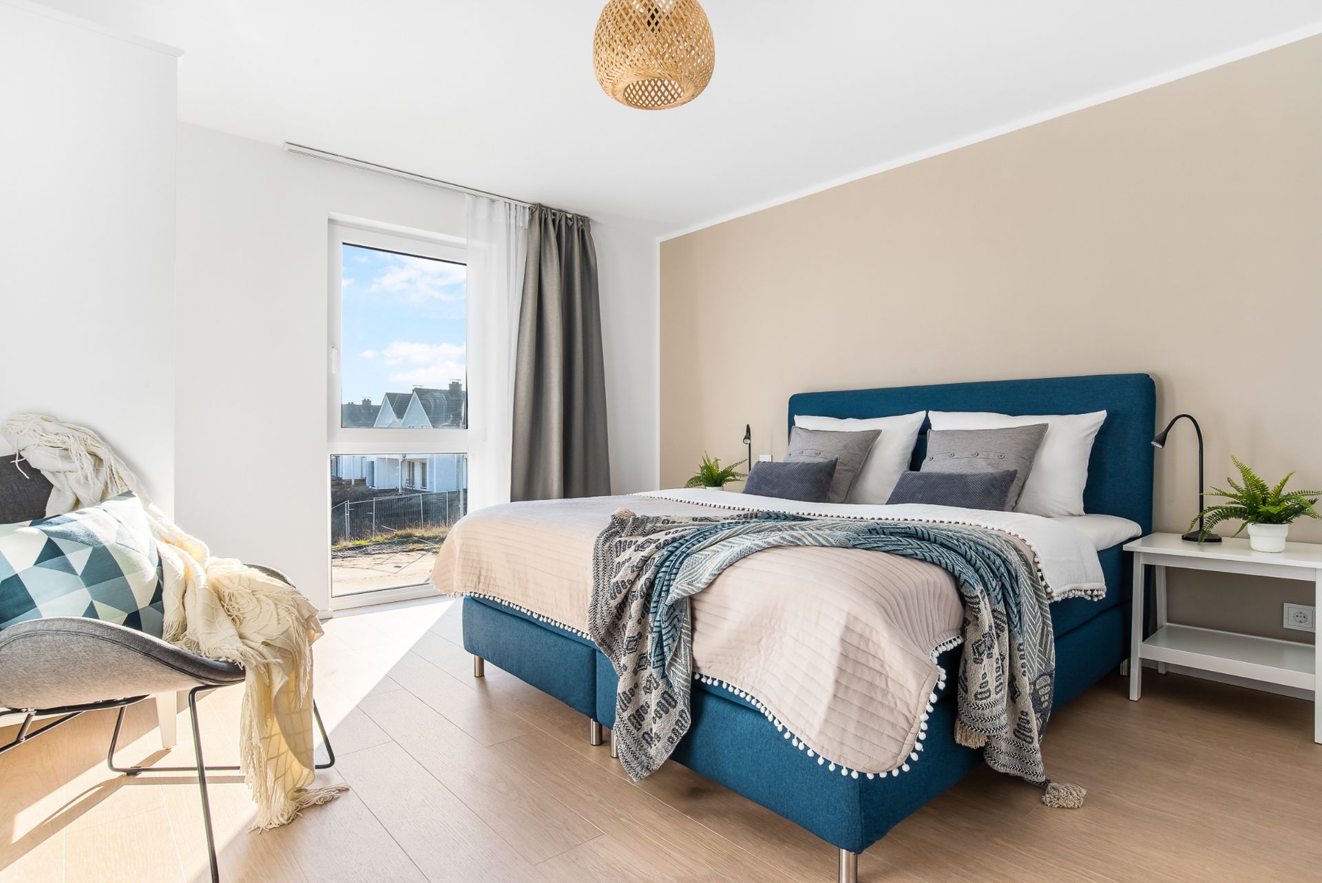 Helles Schlafzimmer mit Doppelbett, Nachttischen, Sessel und großem Fenster.