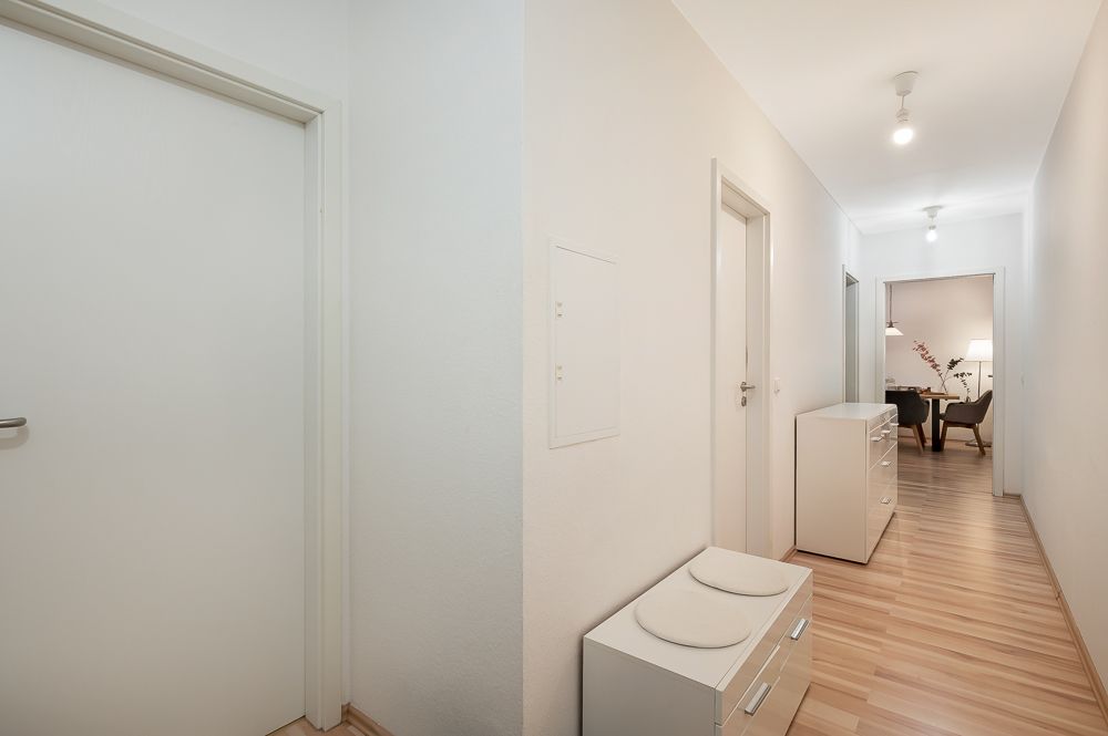Heller Flur mit Holzfußboden, Kommode und Blick in einen Wohnbereich mit Tisch und Stuhl.