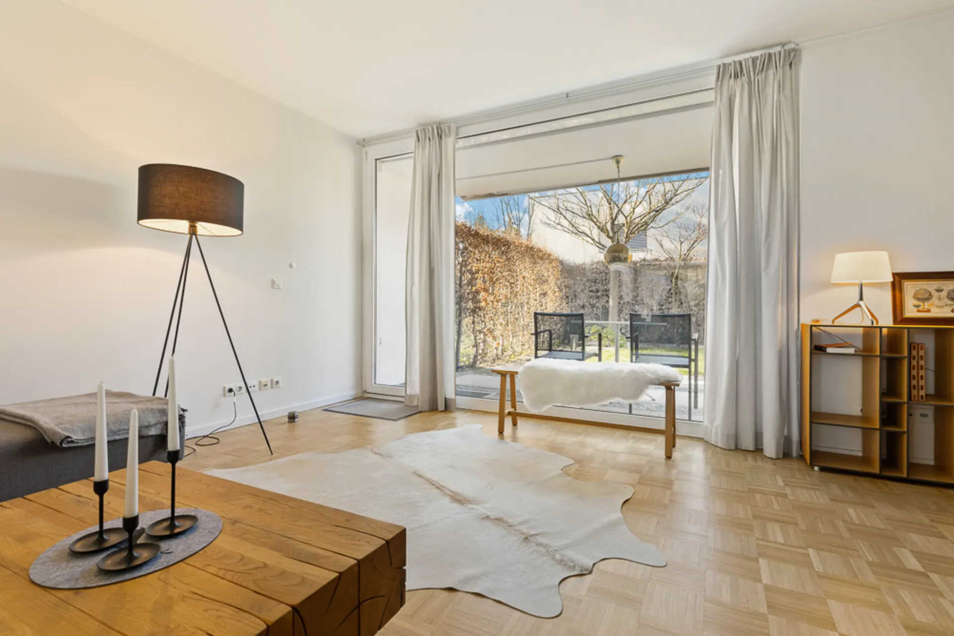 Helles Wohnzimmer mit Holzboden, Stehlampe, Couchtisch und Blick auf Terrasse und Garten.