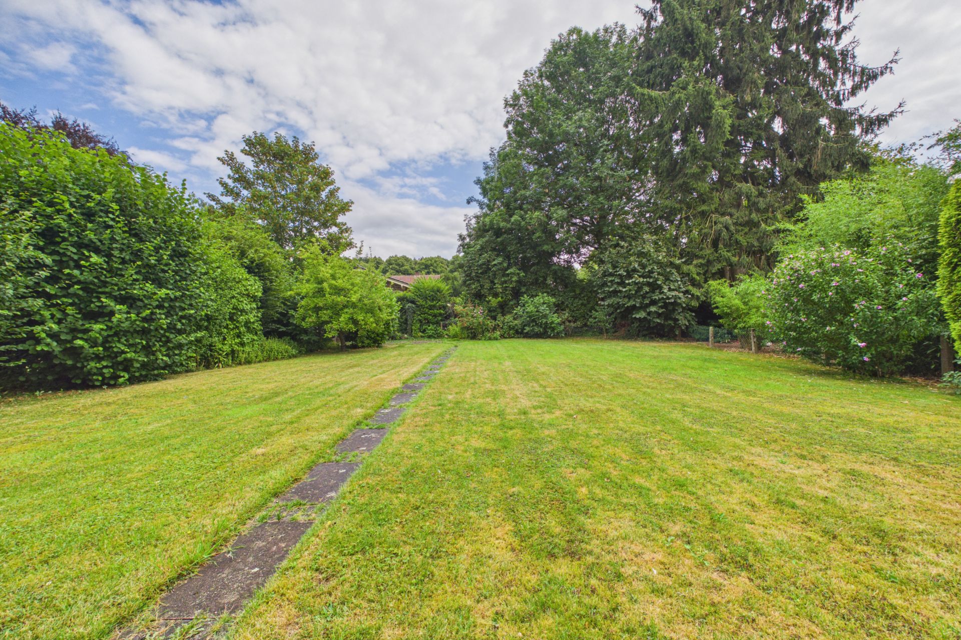 Großer Garten mit Rasenfläche, Gehweg und Bäumen am Rand.