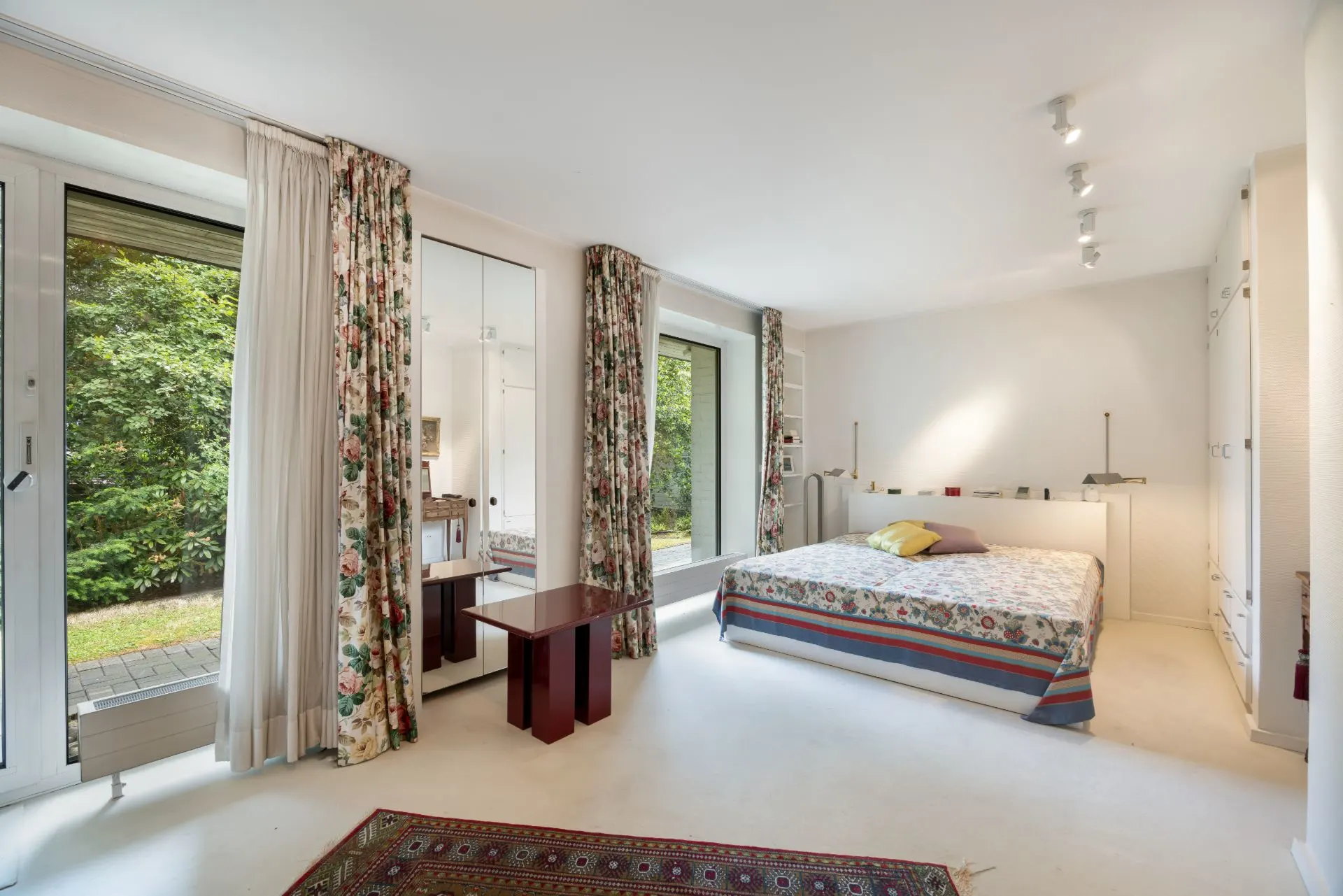 Helles Schlafzimmer mit großem Bett, Fenstern mit Blumenvorhängen und Blick ins Grüne.