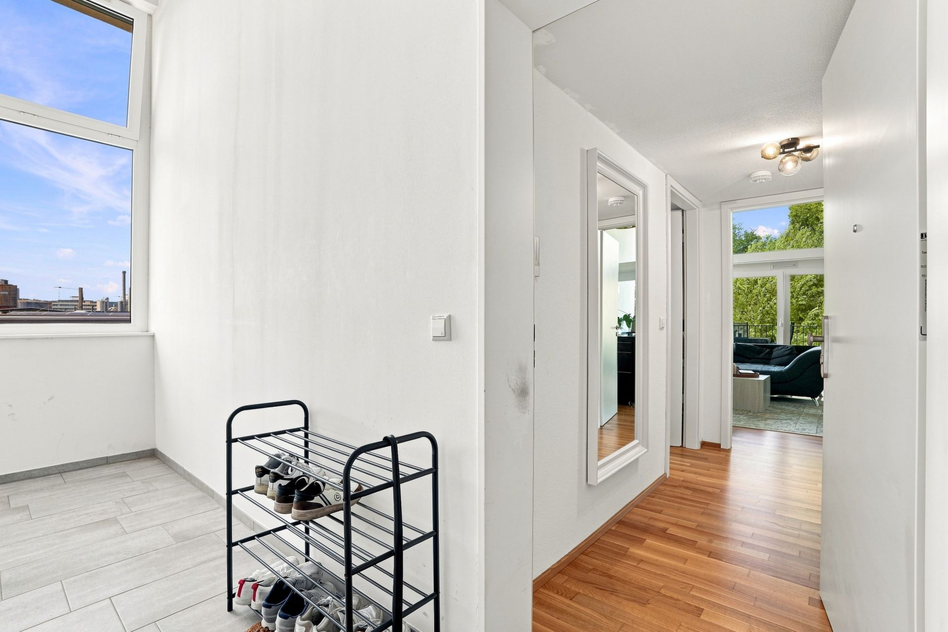 Heller Flur mit Schuhregal, großem Spiegel und Blick ins Wohnzimmer mit großen Fenstern.