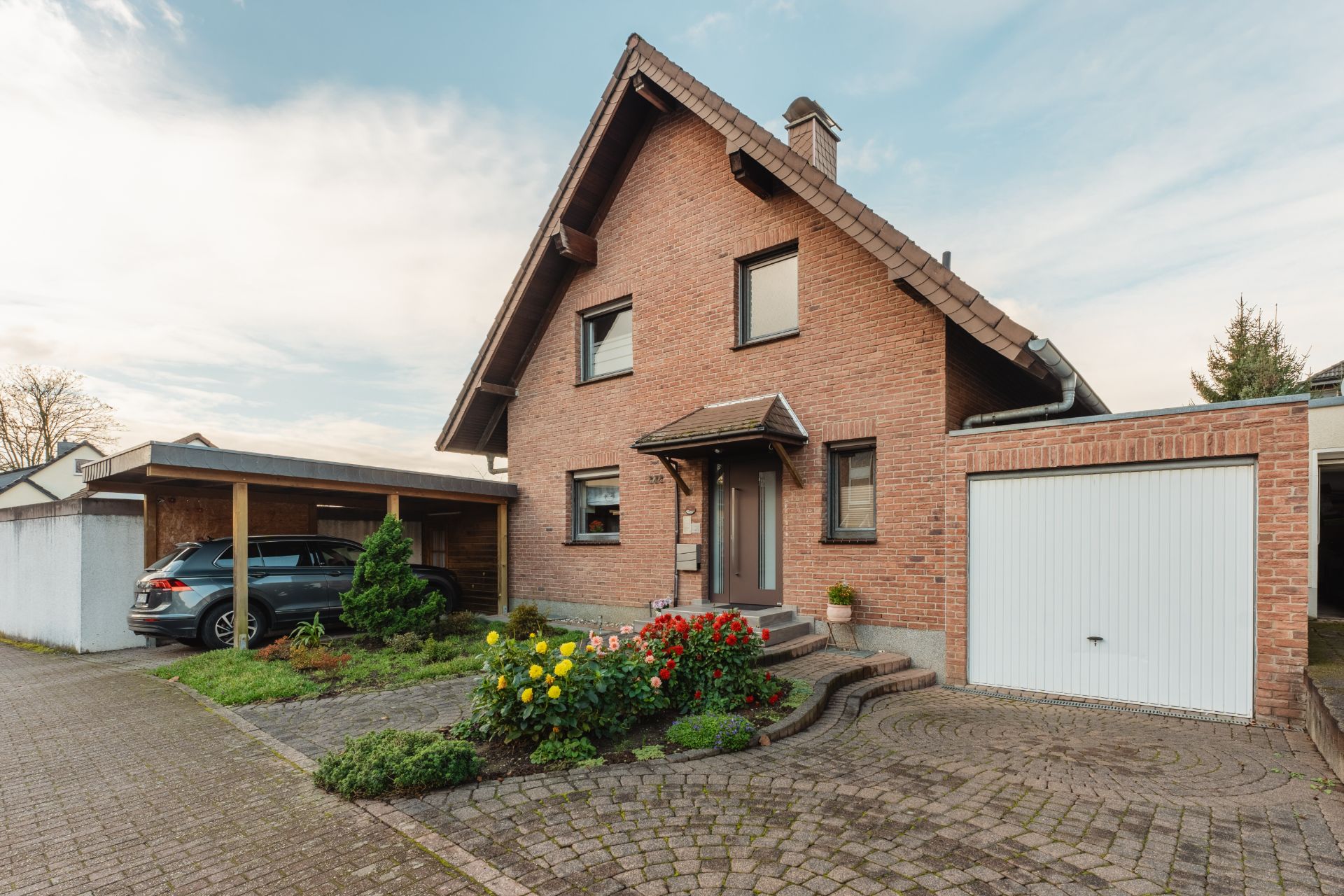 Einfamilienhaus aus Backstein mit Garage, Carport, Vorgarten und Blumenbeet.