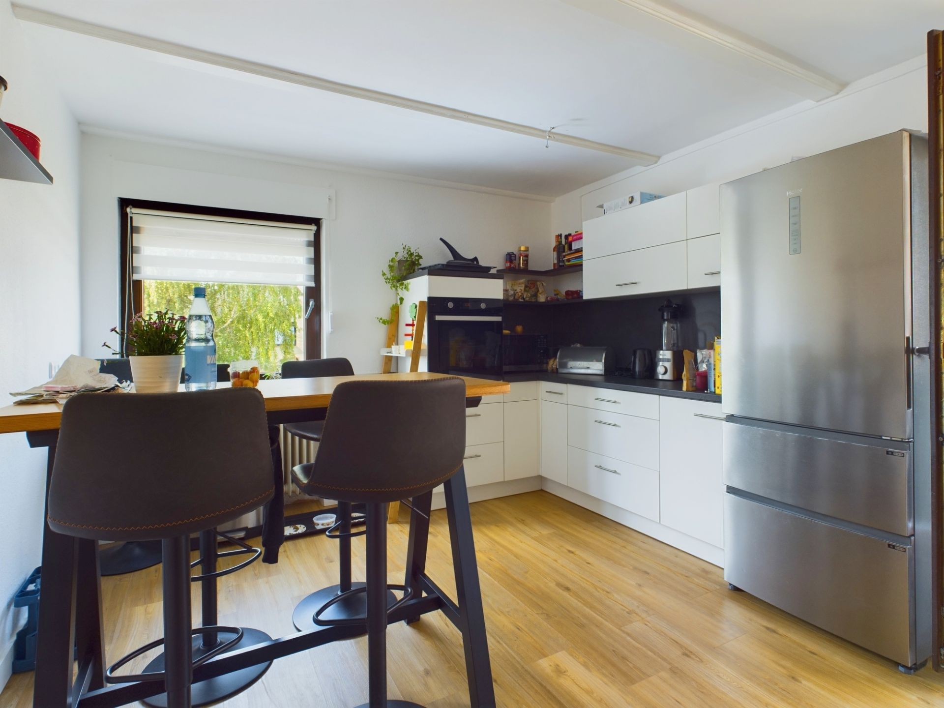 Moderne Küche mit Esstisch, Stühlen, weißen Schränken und großem Edelstahl-Kühlschrank.