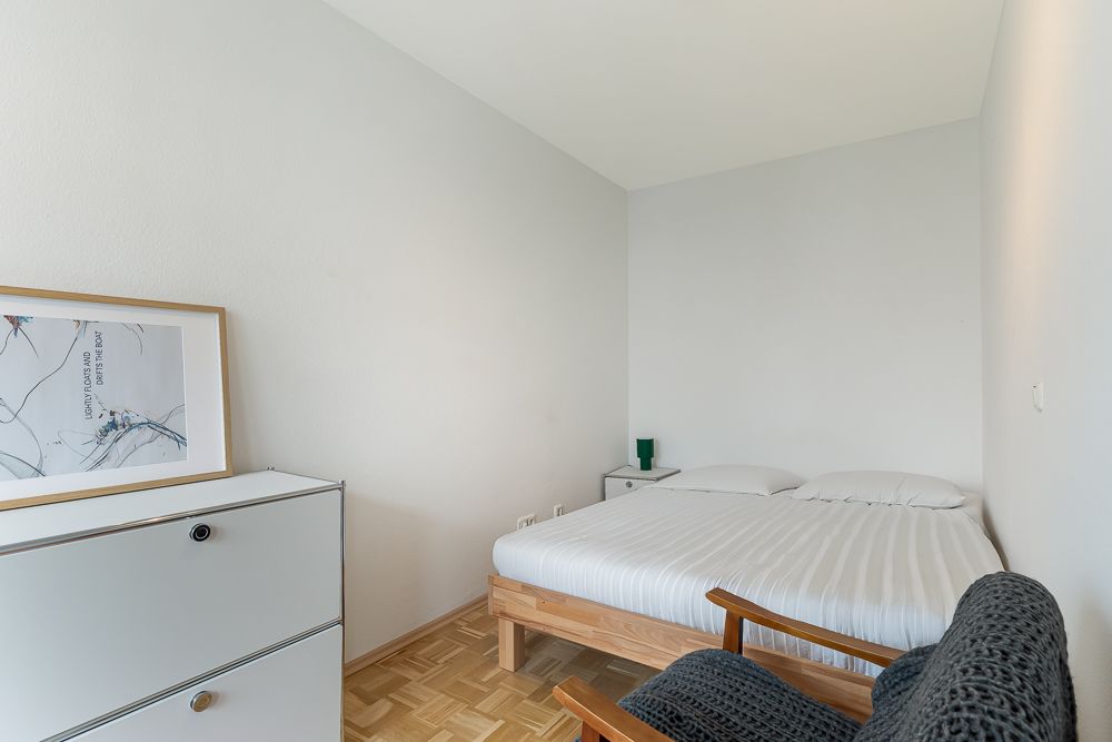 Schlafzimmer mit Doppelbett, Kommode mit Bild, Sessel und Nachttisch auf Parkettboden.