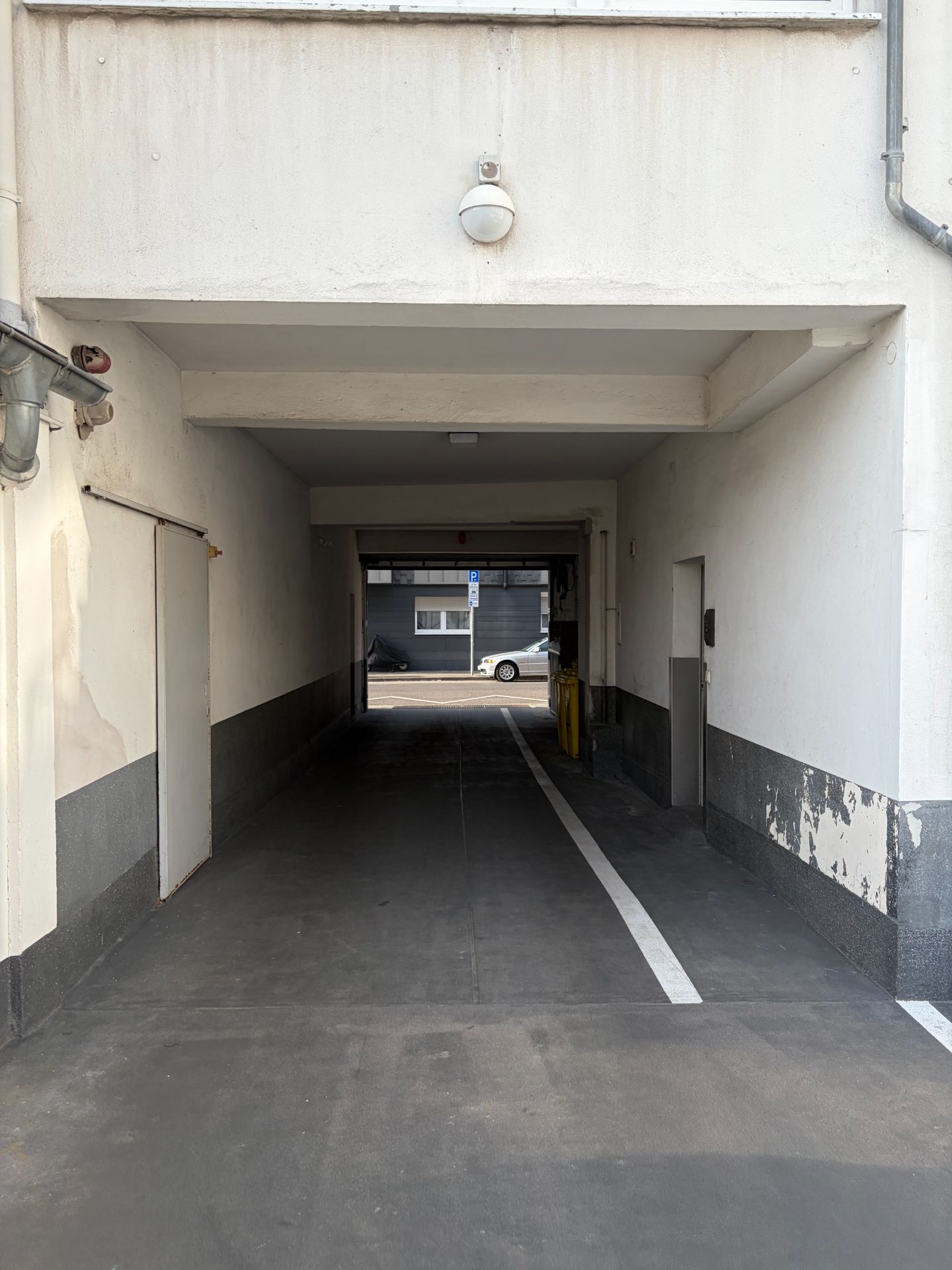 Durchfahrt unter einem Wohnhaus mit heller Wand und Markierung auf dem Boden.