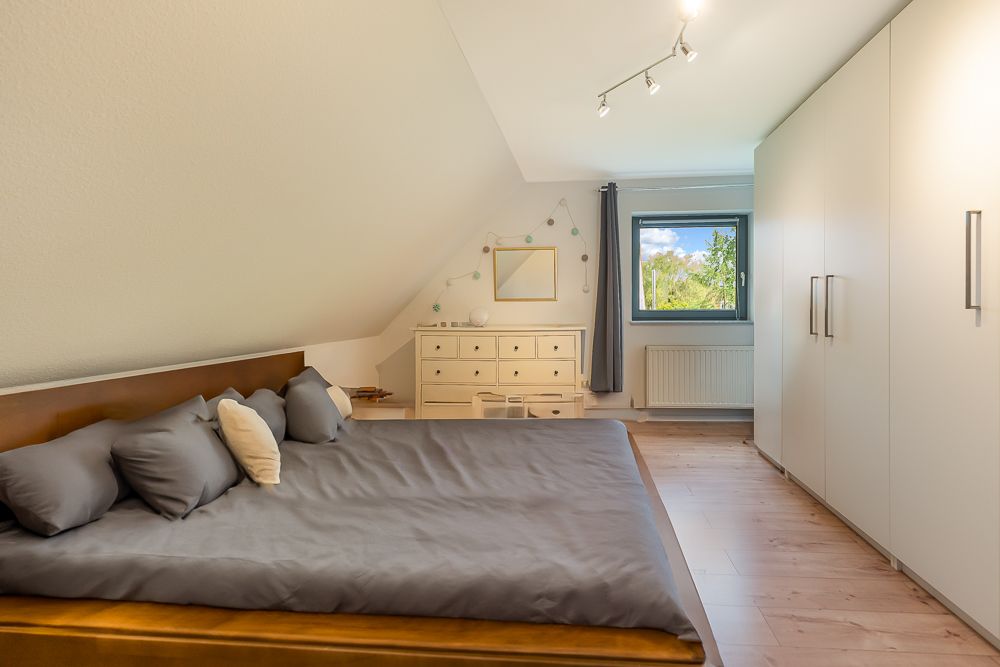 Schlafzimmer mit großem Bett, weißen Schränken, Kommode und Fenster mit Blick nach draußen.