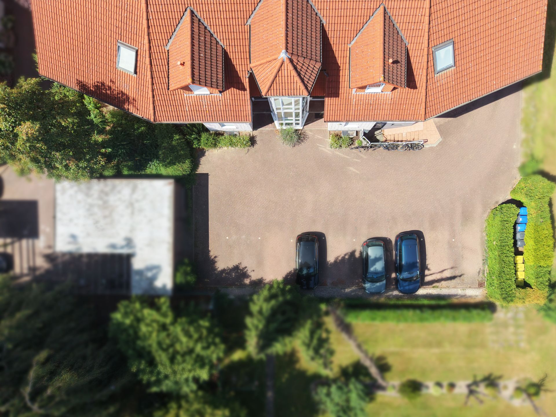 Drohnenaufnahme eines Hauses mit rotem Dach und drei Autos auf dem Hof.