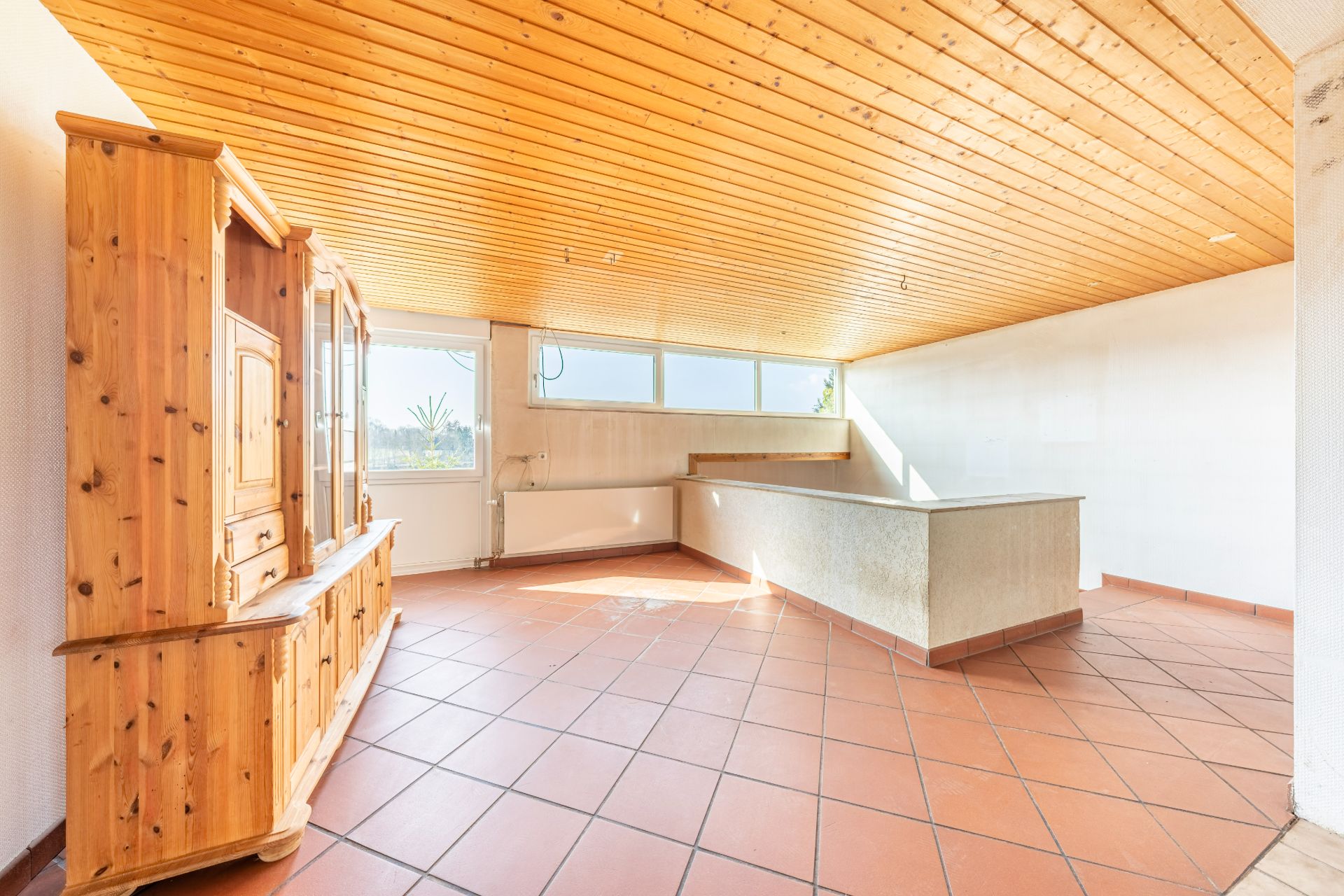 Heller Raum mit Holzdecke, roten Fliesen, Einbauschrank und Theke.