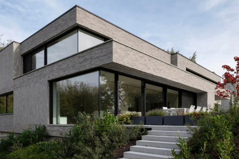Modernes Wohnhaus mit großen Fenstern, Terrasse und umliegendem Garten.