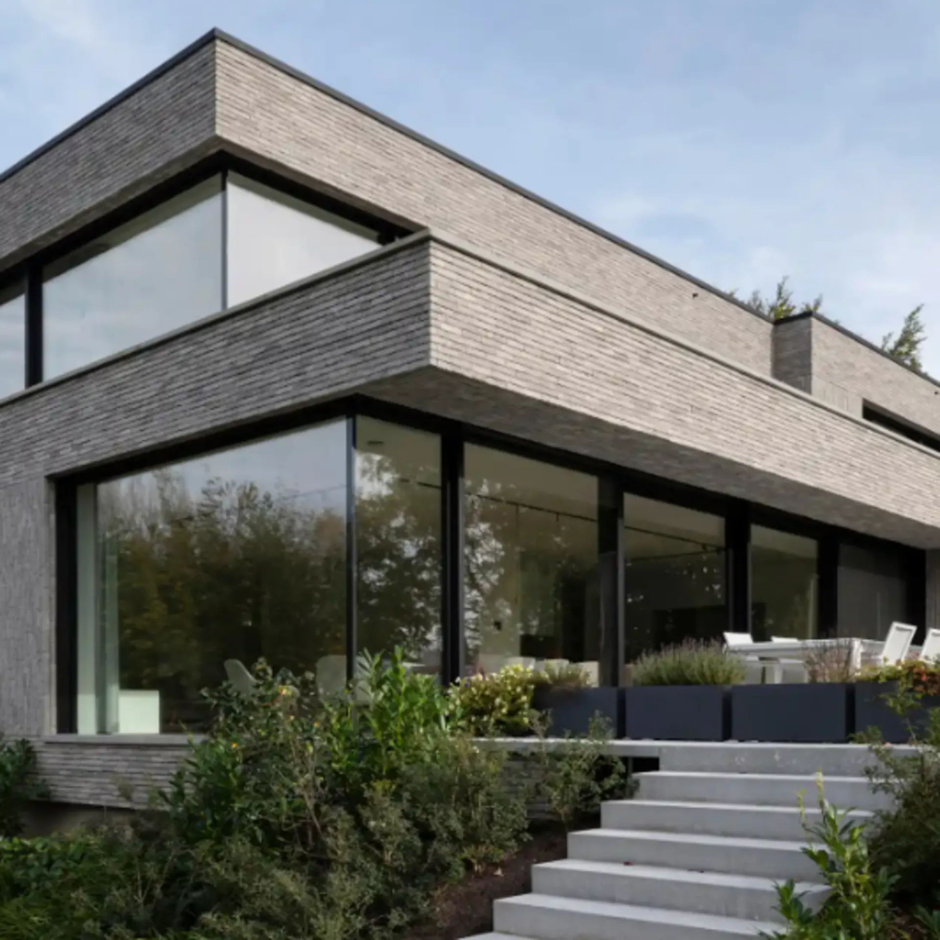 Modernes Wohnhaus mit großen Fenstern, Terrasse und umliegendem Garten.