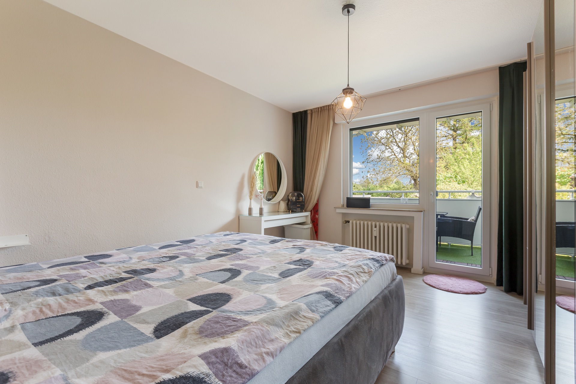 Schlafzimmer mit Doppelbett, Schminktisch, großem Fenster und Zugang zum Balkon.