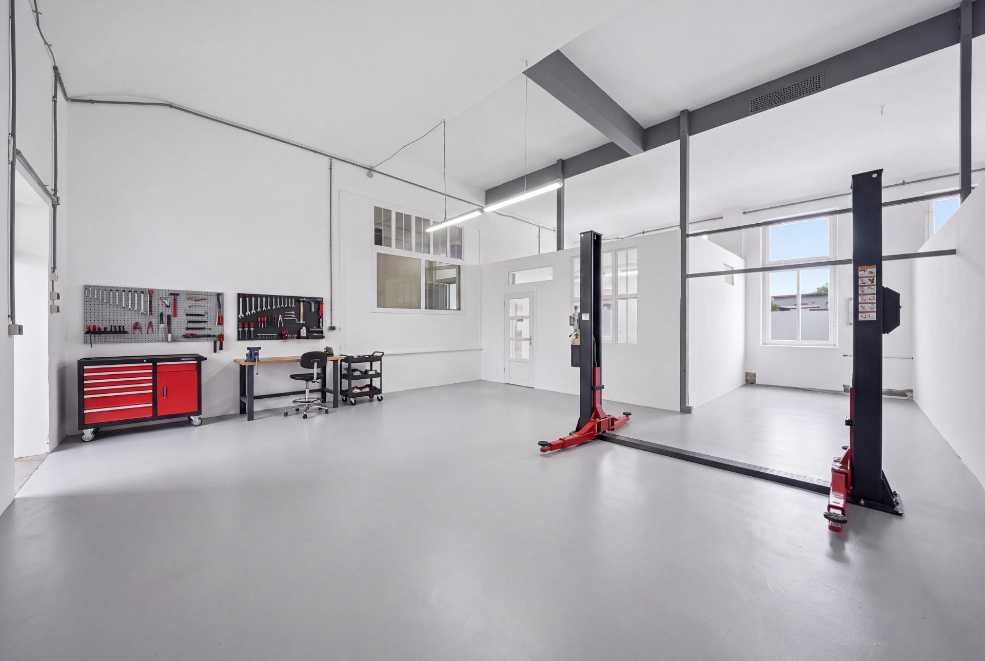Helle Garage mit Hebebühne, Werkbank, Werkzeugwand und großen Fenstern.