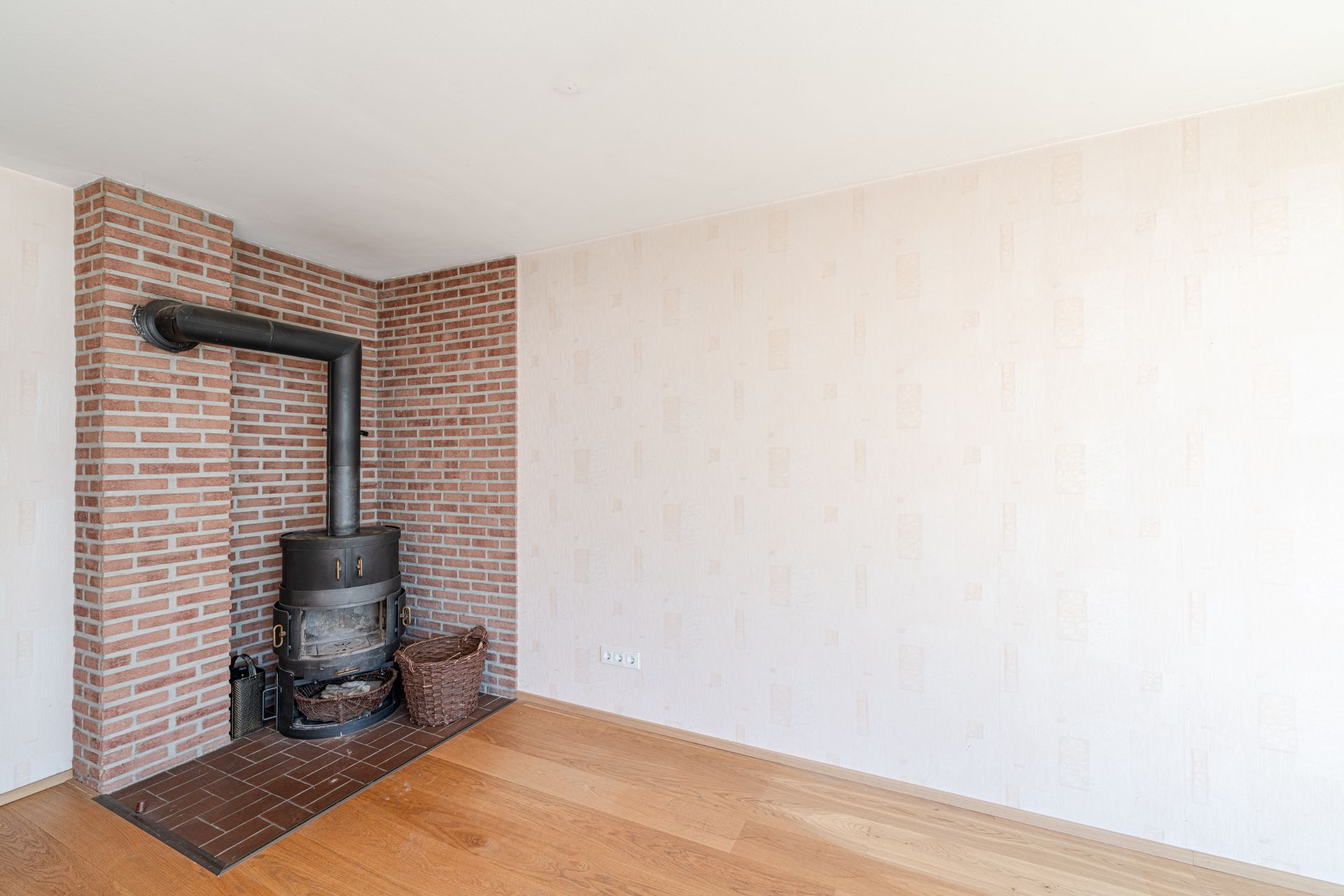 Ecke eines Wohnzimmers mit Kaminofen, Backsteinwand und Holzboden.