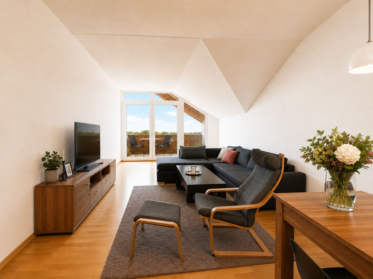 Helles Wohnzimmer mit Ecksofa, Sessel, Fernseher und Zugang zu einem Balkon.