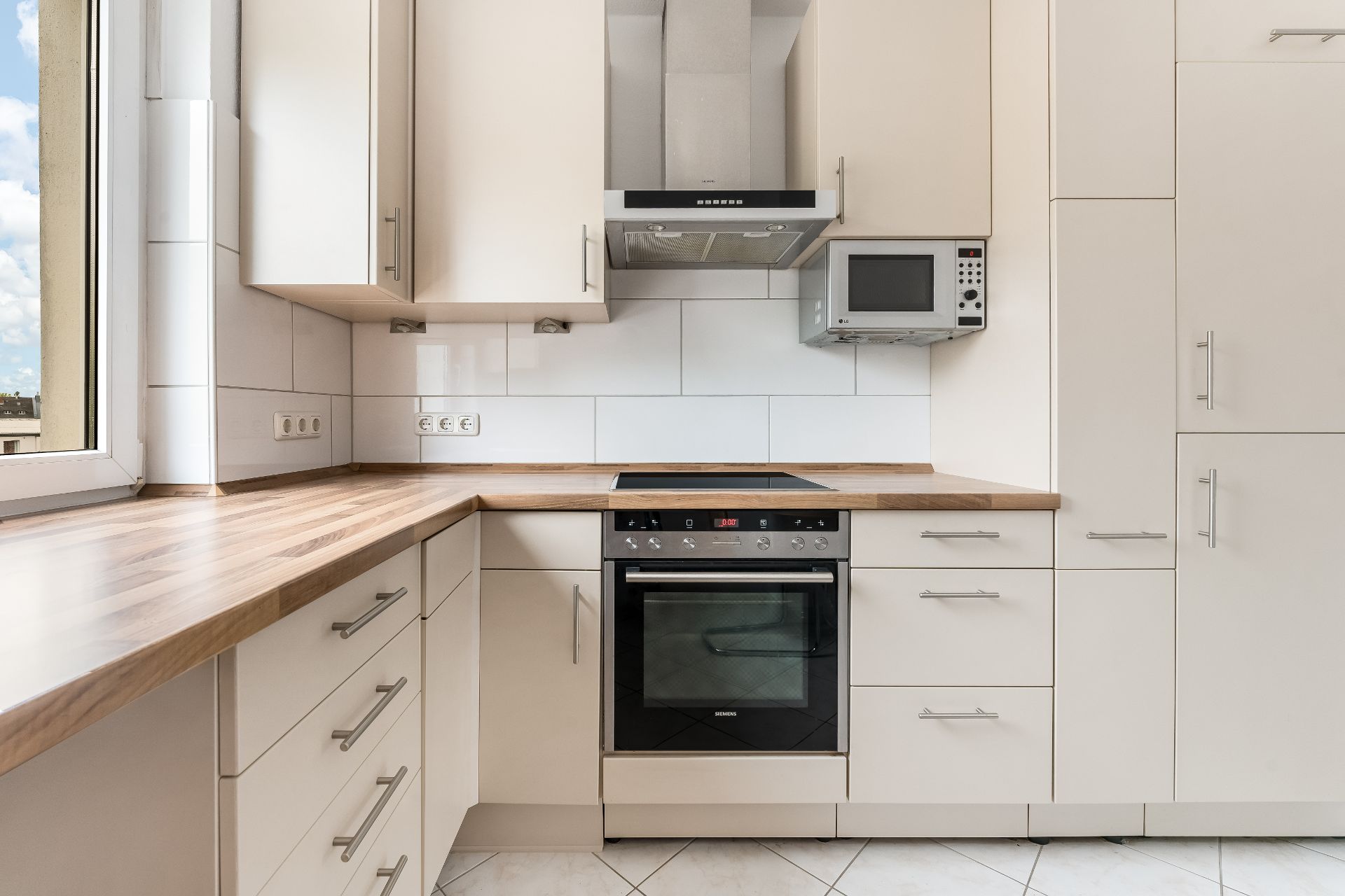 Moderne Einbauküche mit Holzarbeitsplatte, Herd, Backofen, Mikrowelle und weißen Schränken.