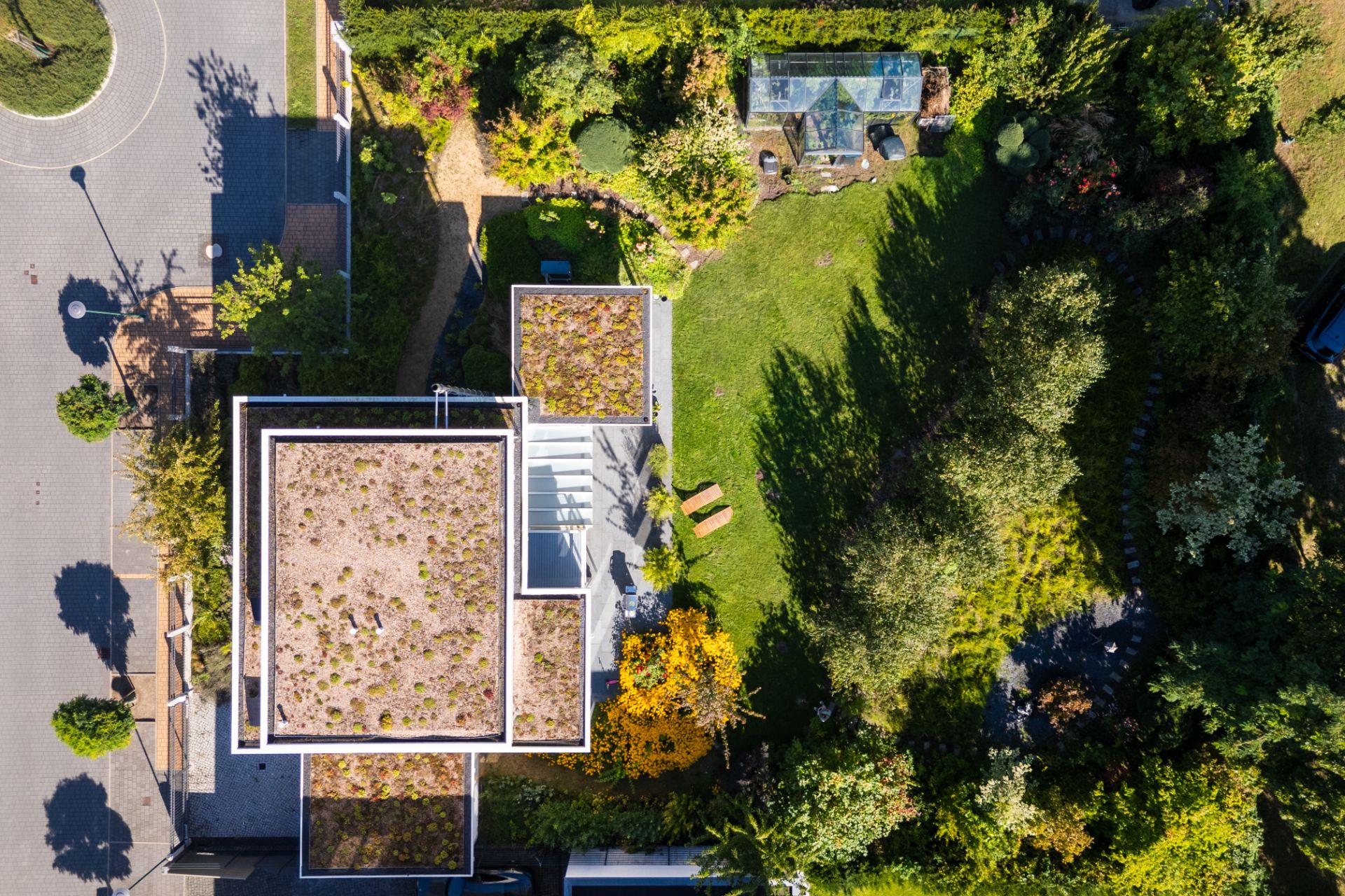 Luftaufnahme eines modernen Hauses mit begrüntem Flachdach und großem Garten mit Bäumen und Wegen.