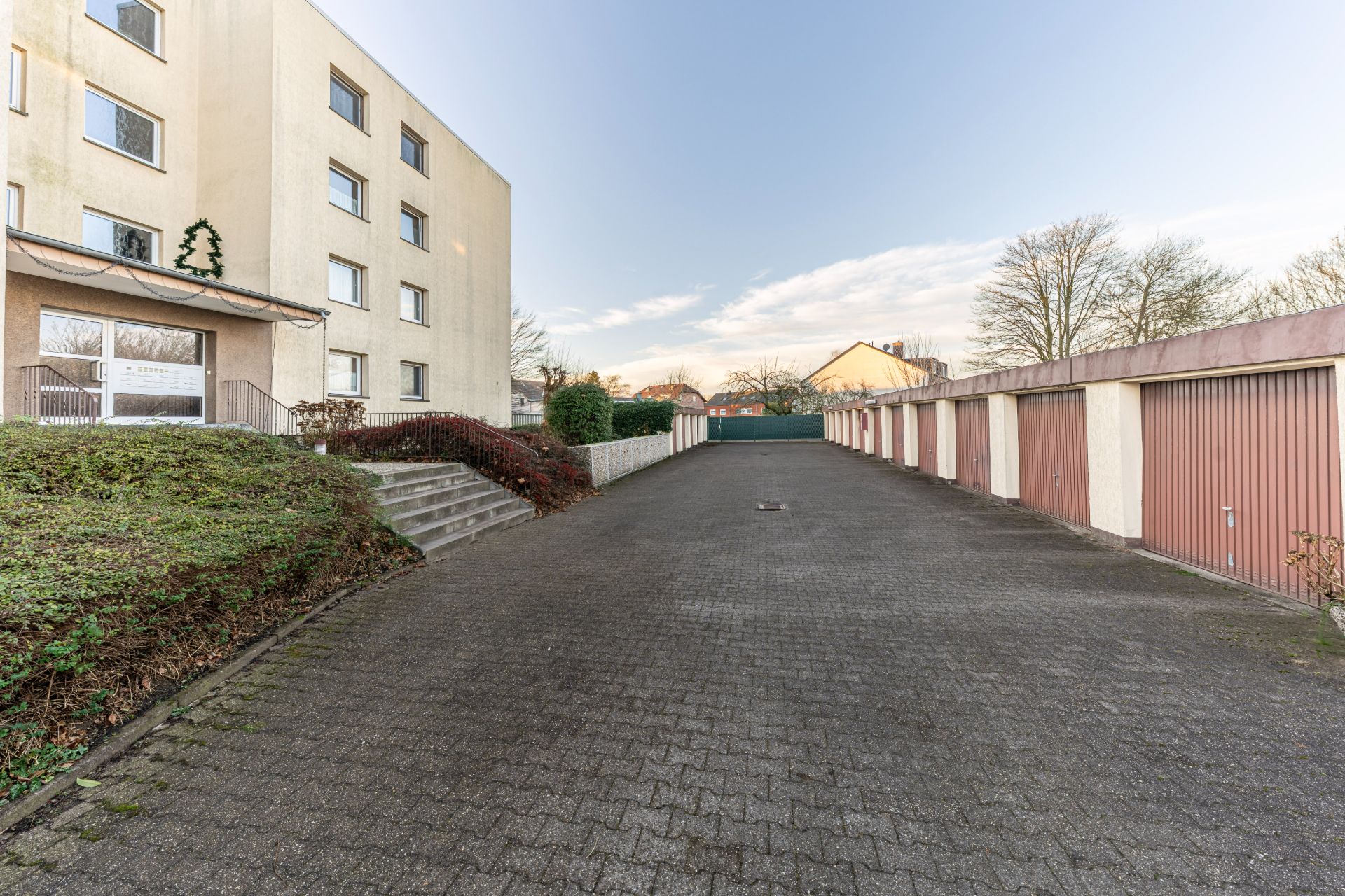 Gepflasterter Hof mit Garagenreihe und mehrstöckigem Wohnhaus links.
