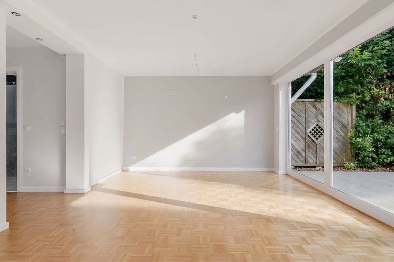 Heller, leerer Raum mit Parkettboden und großer Fensterfront zum Garten.