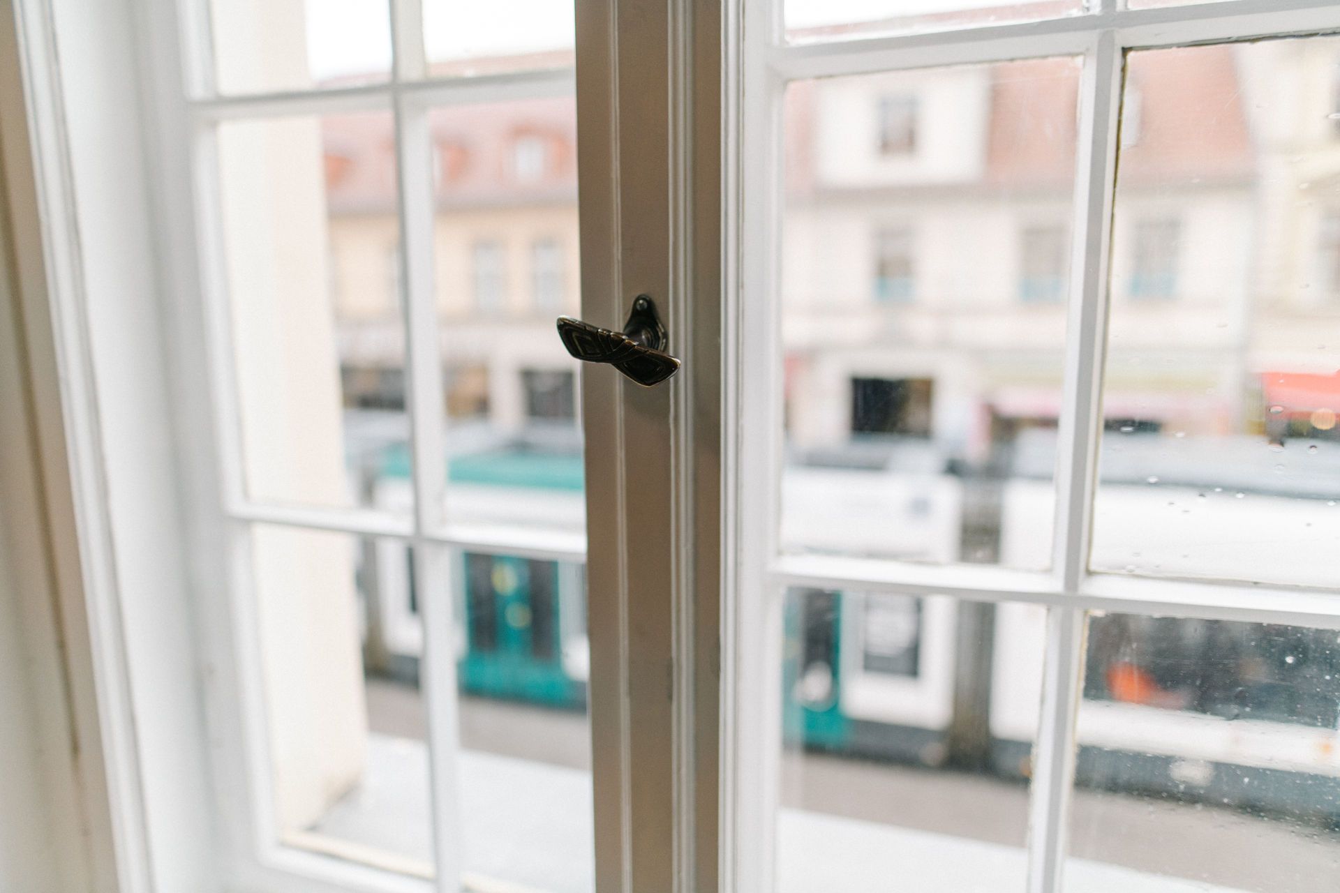 Nahaufnahme eines weißen Fensters mit Griff, Blick auf unscharfe Straße und Gebäude.
