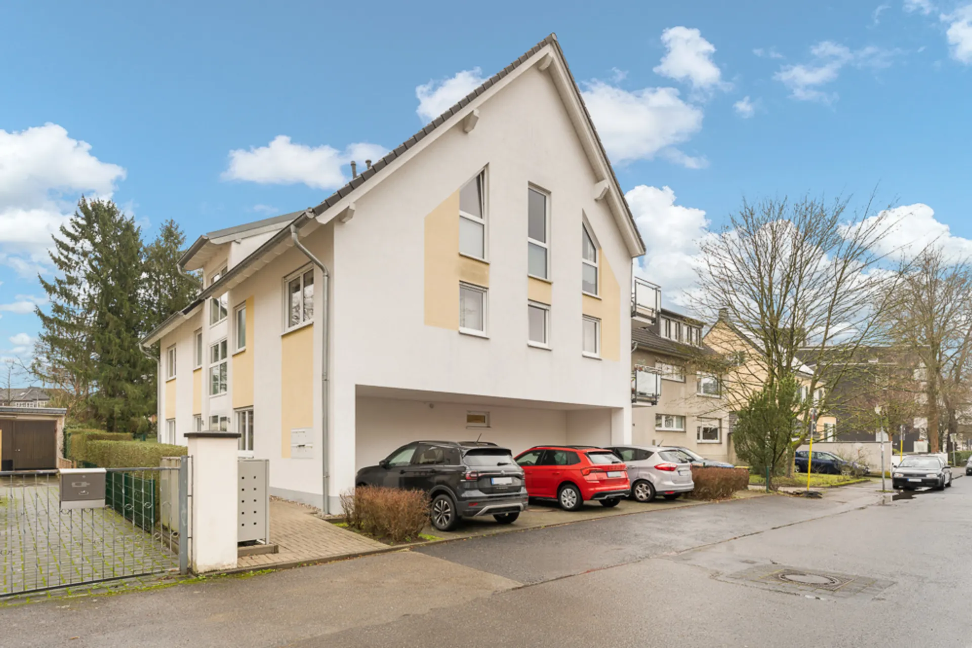 Modernes Wohnhaus mit Satteldach und mehreren geparkten Autos vor dem Gebäude.