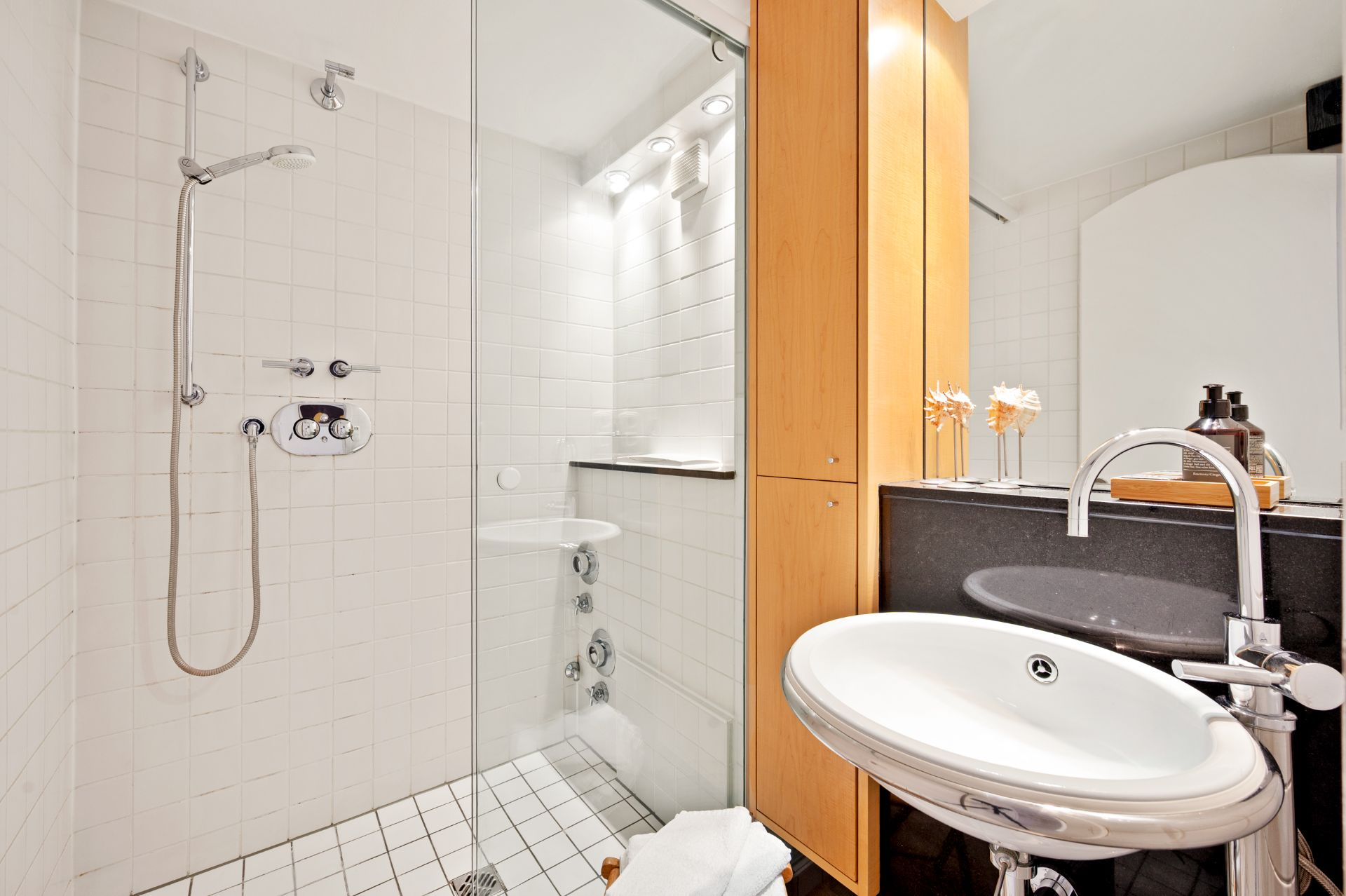 Modernes Badezimmer mit Dusche, Waschbecken, Spiegelschrank und hellen Fliesen.