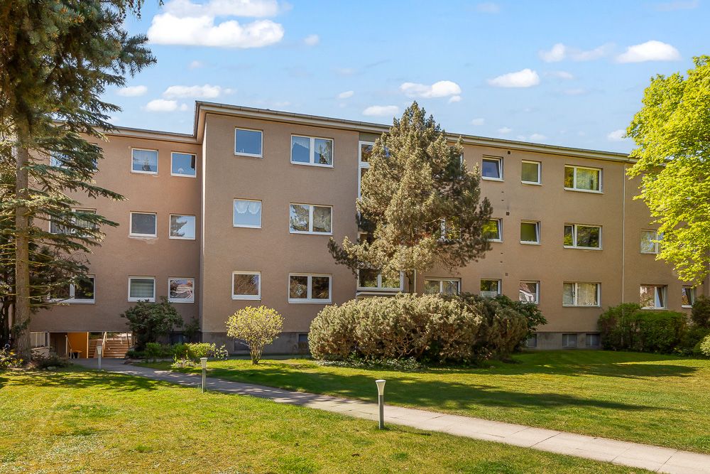 Dreistöckiges Wohnhaus mit vielen Fenstern, umgeben von Bäumen und gepflegtem Rasen.
