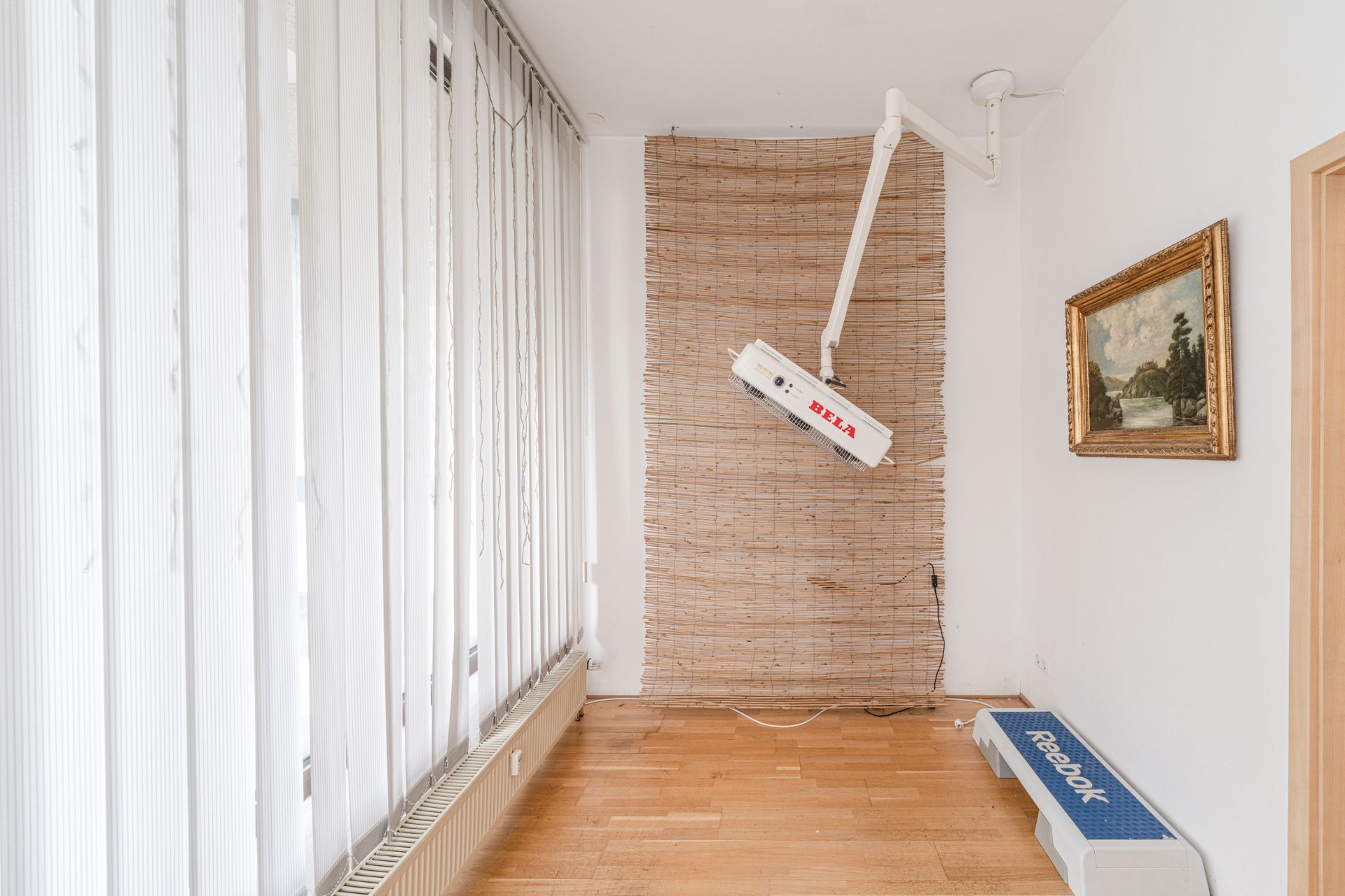 Heller Raum mit Holzfußboden, Lamellenjalousien, Wandgerät, Bild und Reebok-Stepper.