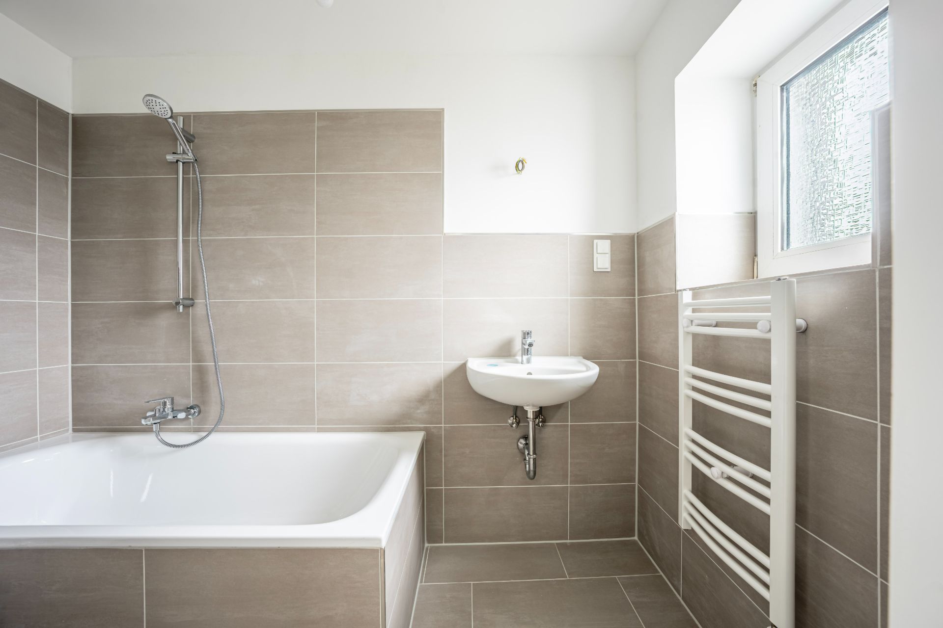 Modernes Badezimmer mit Badewanne, Wandwaschbecken, Fenster und Handtuchheizkörper.