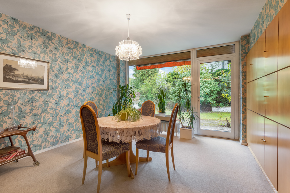Esszimmer mit rundem Tisch, vier Stühlen, Blumenmuster-Tapete und Blick auf den Garten.