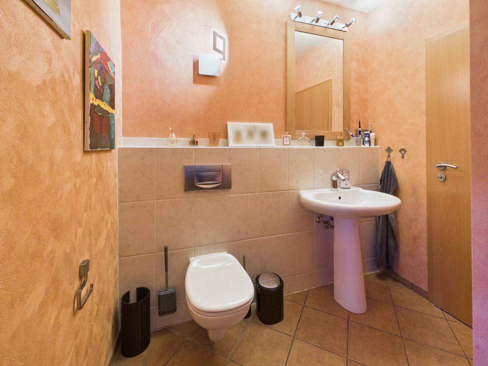 Modernes Badezimmer mit Wandtoilette, Waschbecken, Spiegel und Handtuch an der Wand.