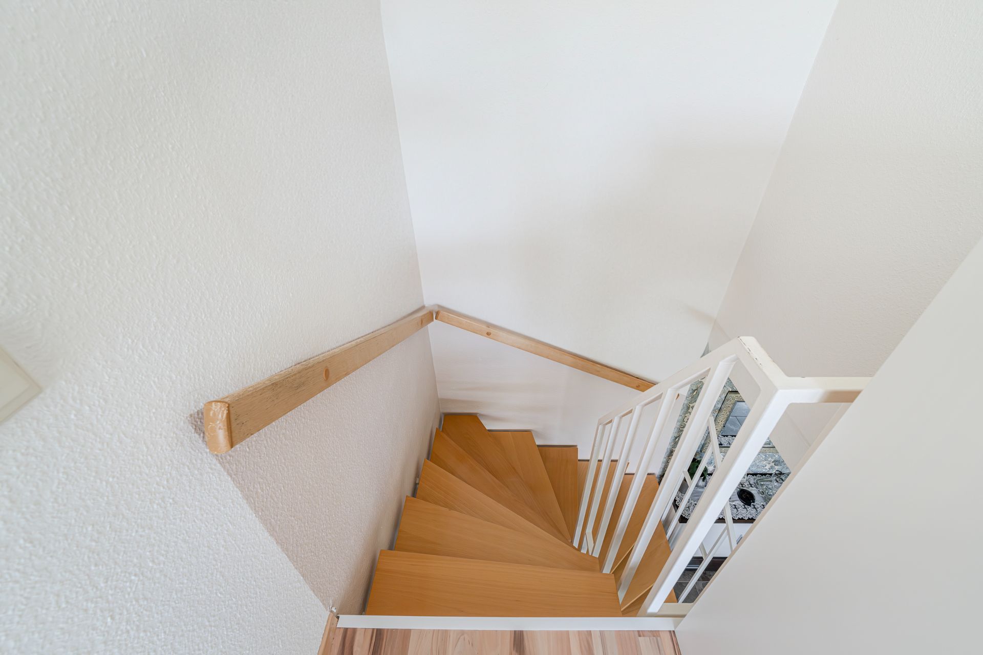 Holztreppe mit weißem Geländer und Handlauf an einer weißen Wand.
