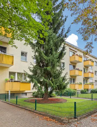 Mehrfamilienhaus mit gelben Balkonen, grünem Vorgarten und Einfahrtstor.