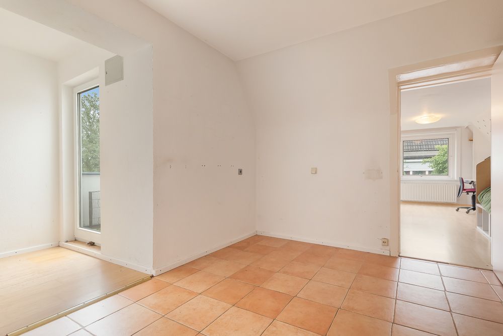 Leerer Raum mit Fliesenboden, angrenzendem Fenster und Durchgang zu einem weiteren Zimmer.