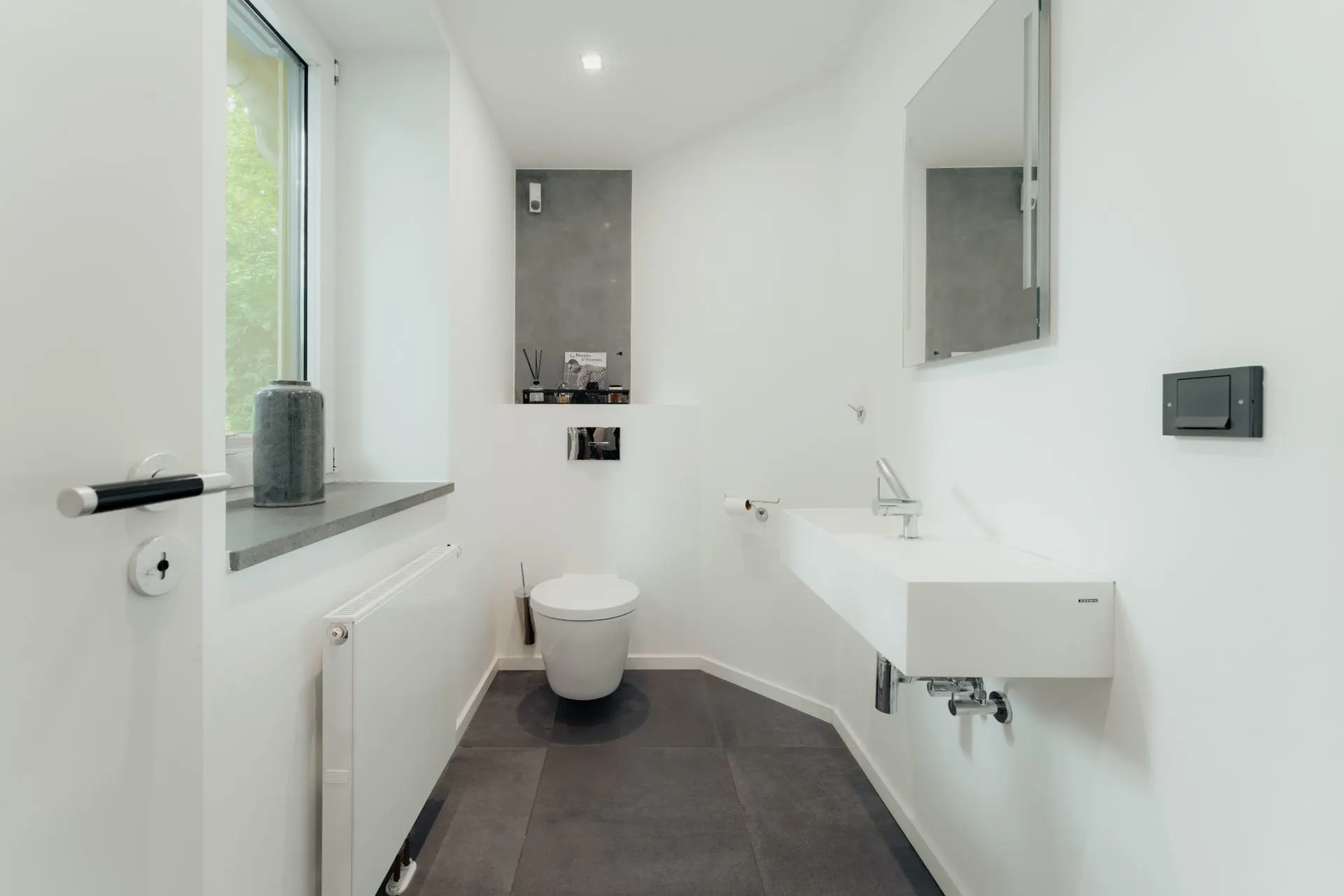 Modernes Badezimmer mit WC, Waschbecken und Fenster, gestaltet in Weiß und Grau.