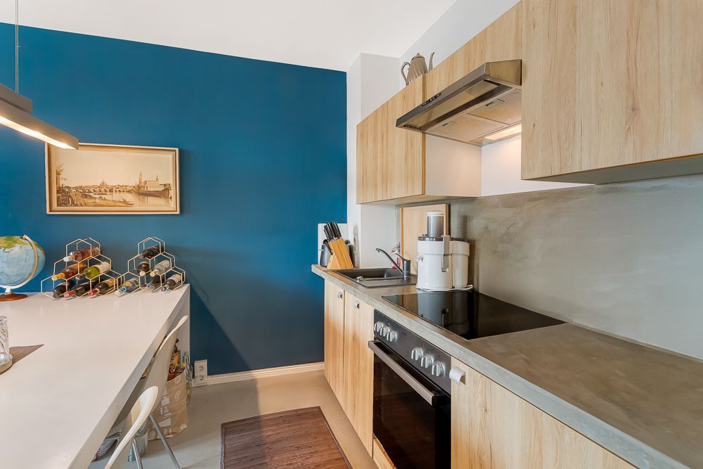 Moderne Küche mit Holzfronten, blau gestrichener Wand und Küchengeräten auf der Arbeitsplatte.