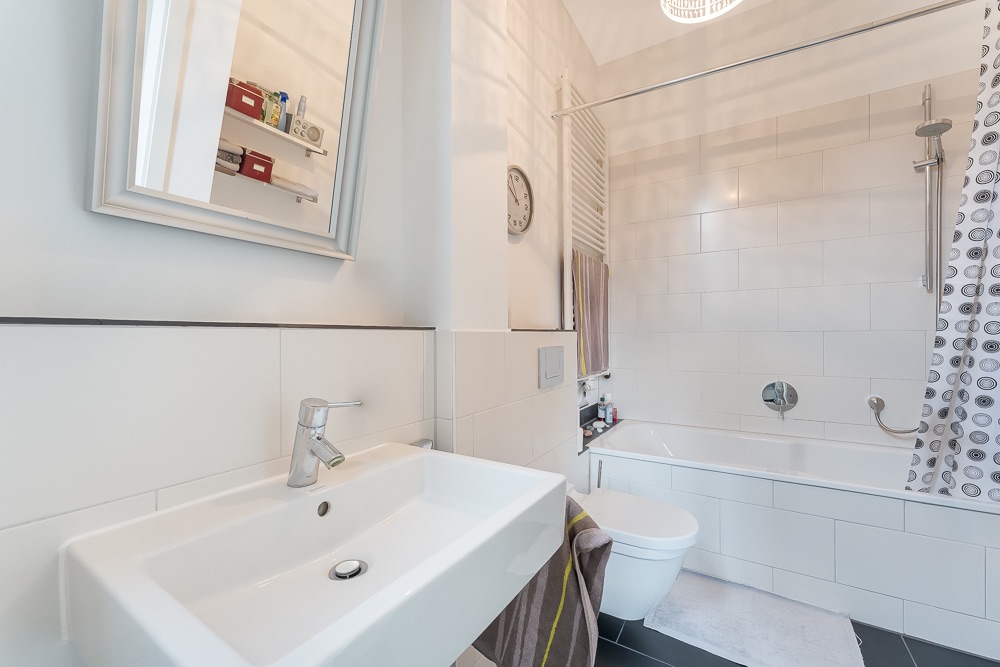 Modernes Badezimmer mit Waschbecken, Spiegel, Badewanne, WC und Duschvorhang.