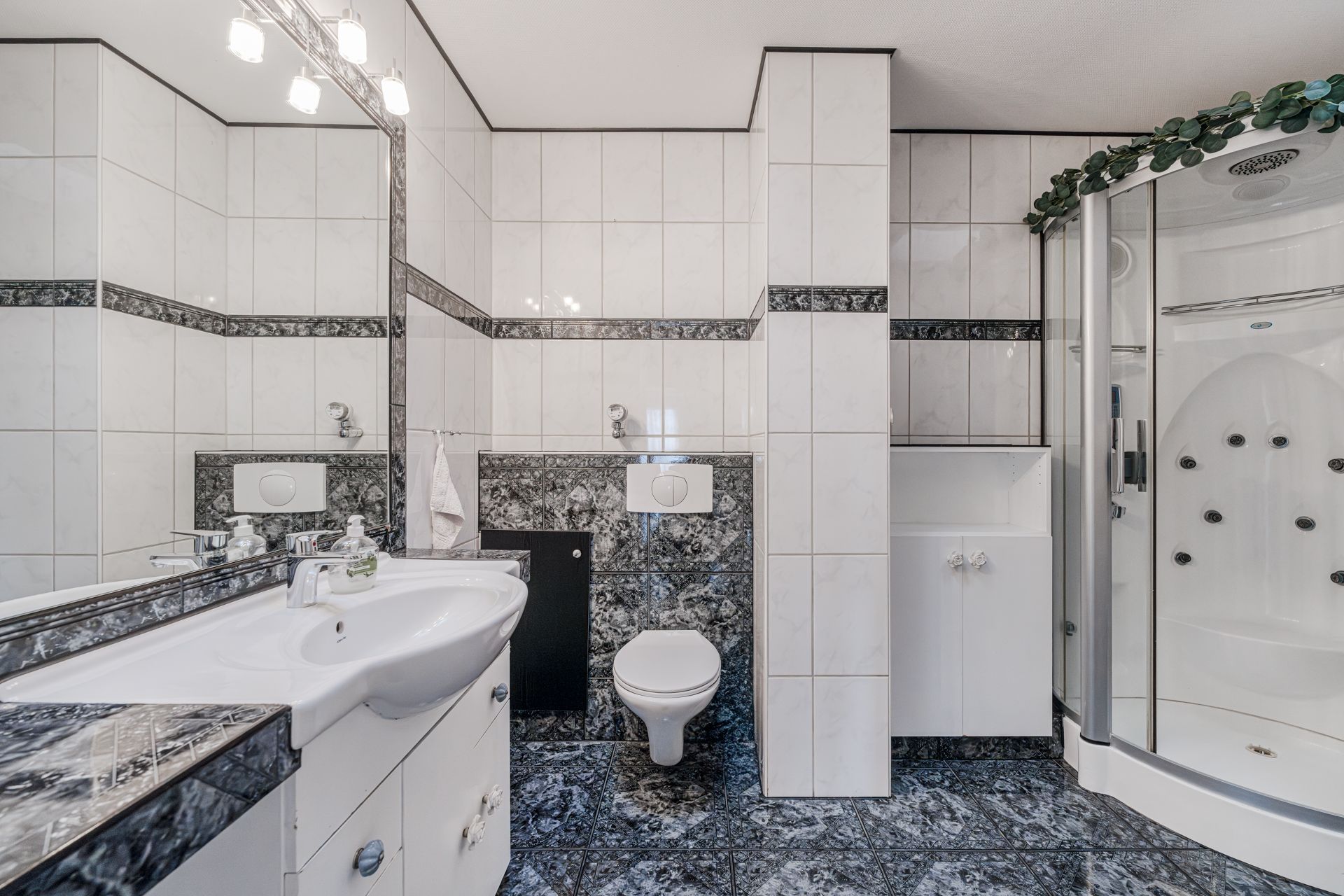 Modernes Bad mit Dusche, Waschbecken, Spiegel, Toilette und weißen Fliesen mit dunklen Akzenten.